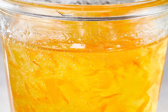 Close-up of a glass filled with orange marmalade, showing its thick, chunky texture and pieces of orange peel suspended in the jelly-like spread.