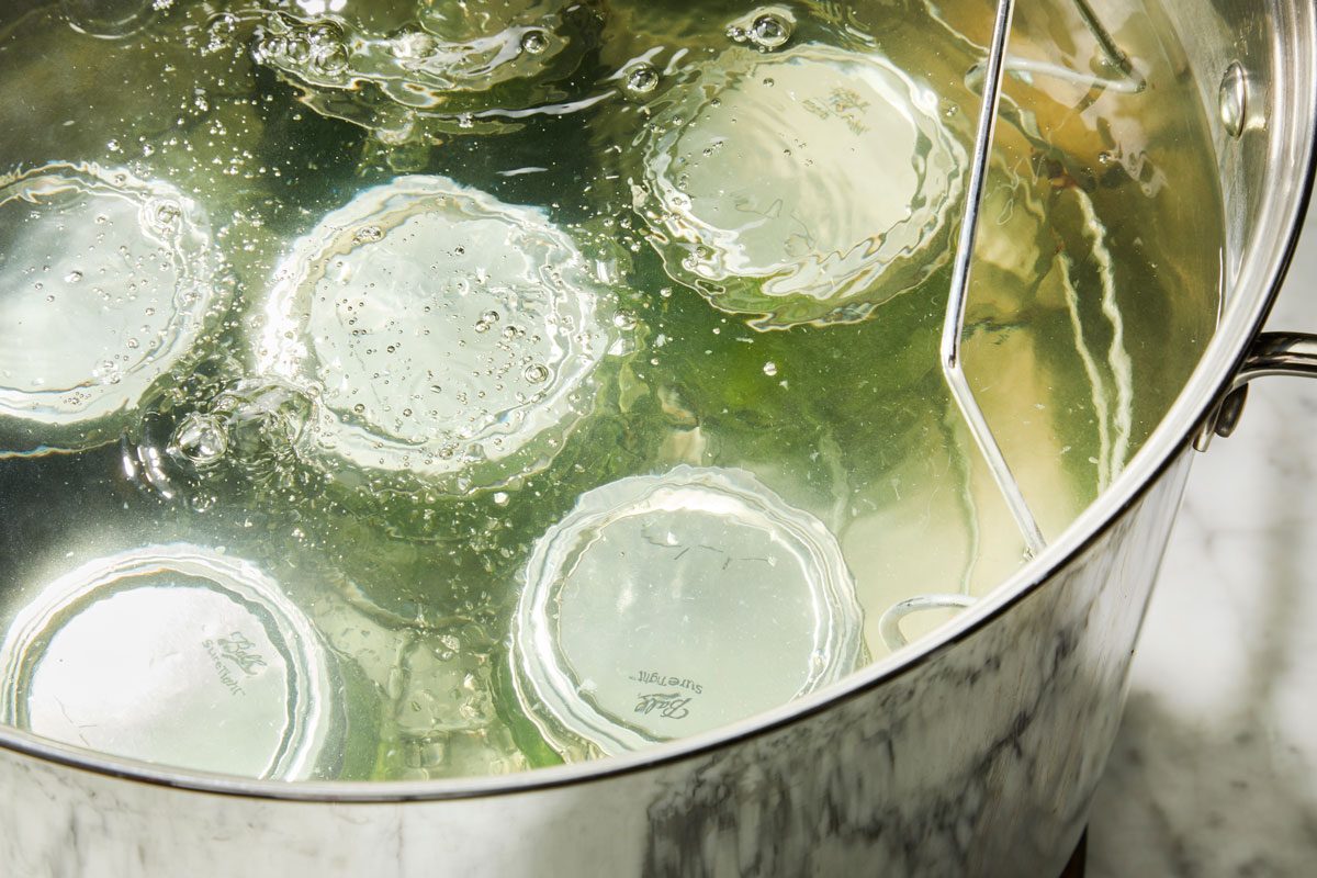 High angle view shot of center lids on jars; screw on bands until fingertip tight; Place jars in canner with simmering water ensuring that they are completely covered with water; Bring to a boil; process 10 minutes; marble surface;