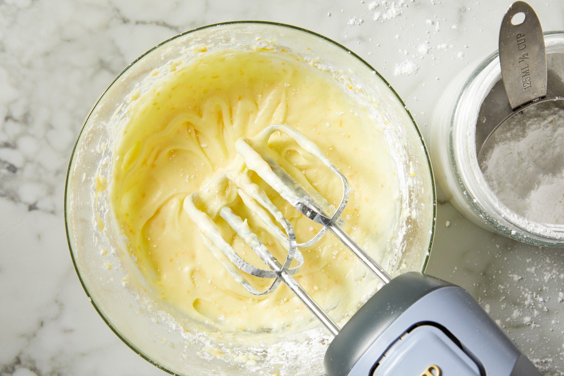Overhead shot; For frosting beat butter; cream cheese; orange juice; zest and salt until blended; gradually beat in confectioners’ sugar; Spread over tops; Refrigerate leftovers; marble surface;