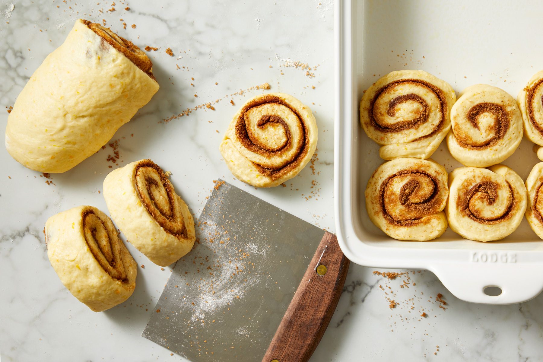 Overhead shot of roll up jelly-roll style; starting with a long side; pinch seam to seal; Cut into 12 slices; place in a greased 13x9-inch pan; cut side down; marble surface;