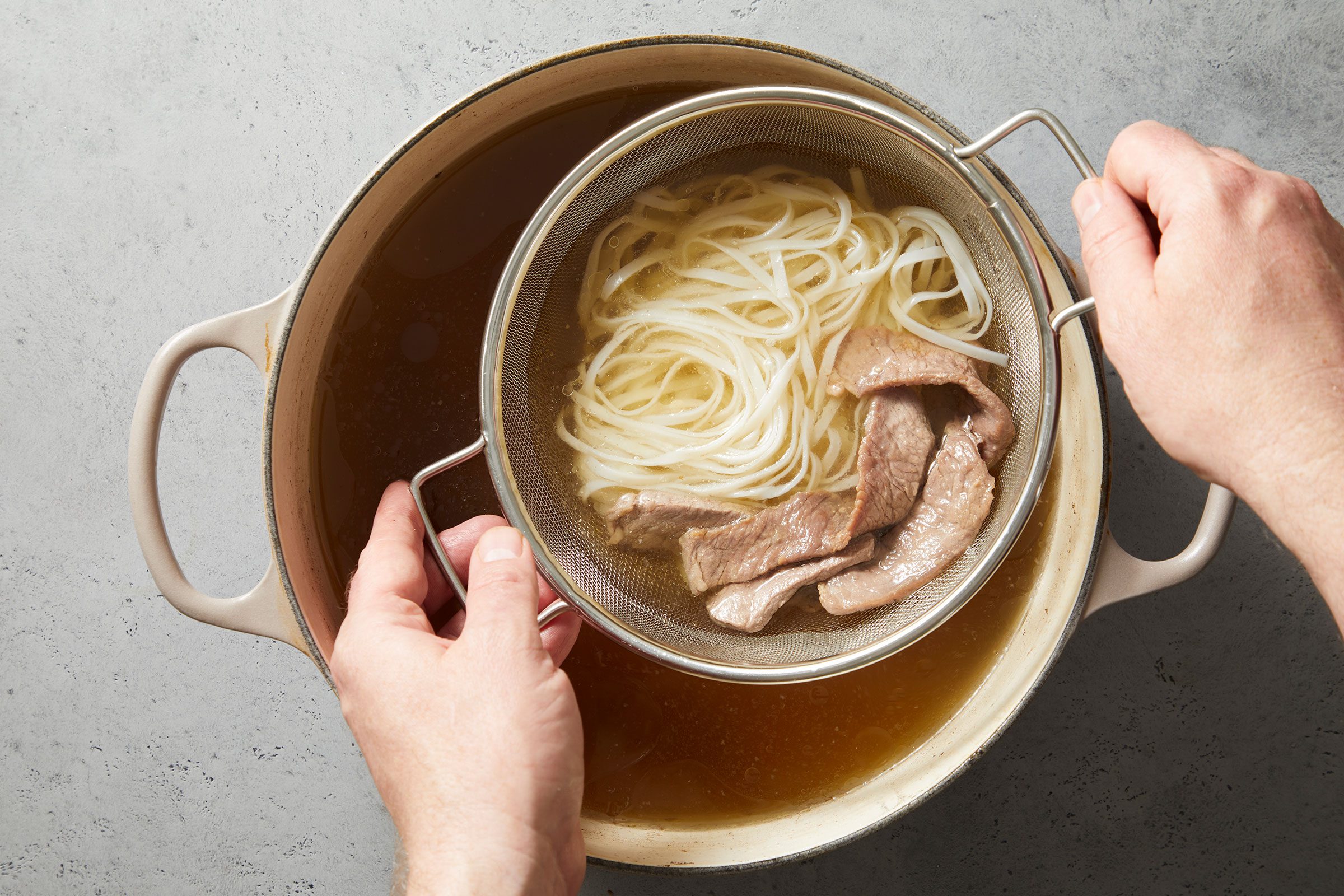 An individual portion of noodles and beef added to a small colander for one portion