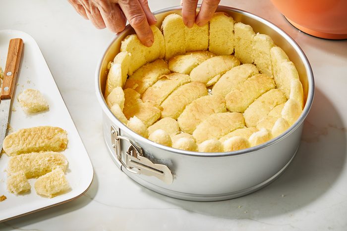 3/4 angle view shot; Place ladyfingers around the sides and on the bottom of a greased 9 inch springform pan; marble surface;