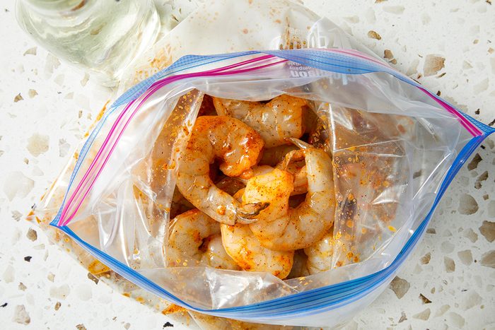 Raw shrimp marinated with spices inside a partially opened resealable plastic bag, placed on a white terrazzo countertop.