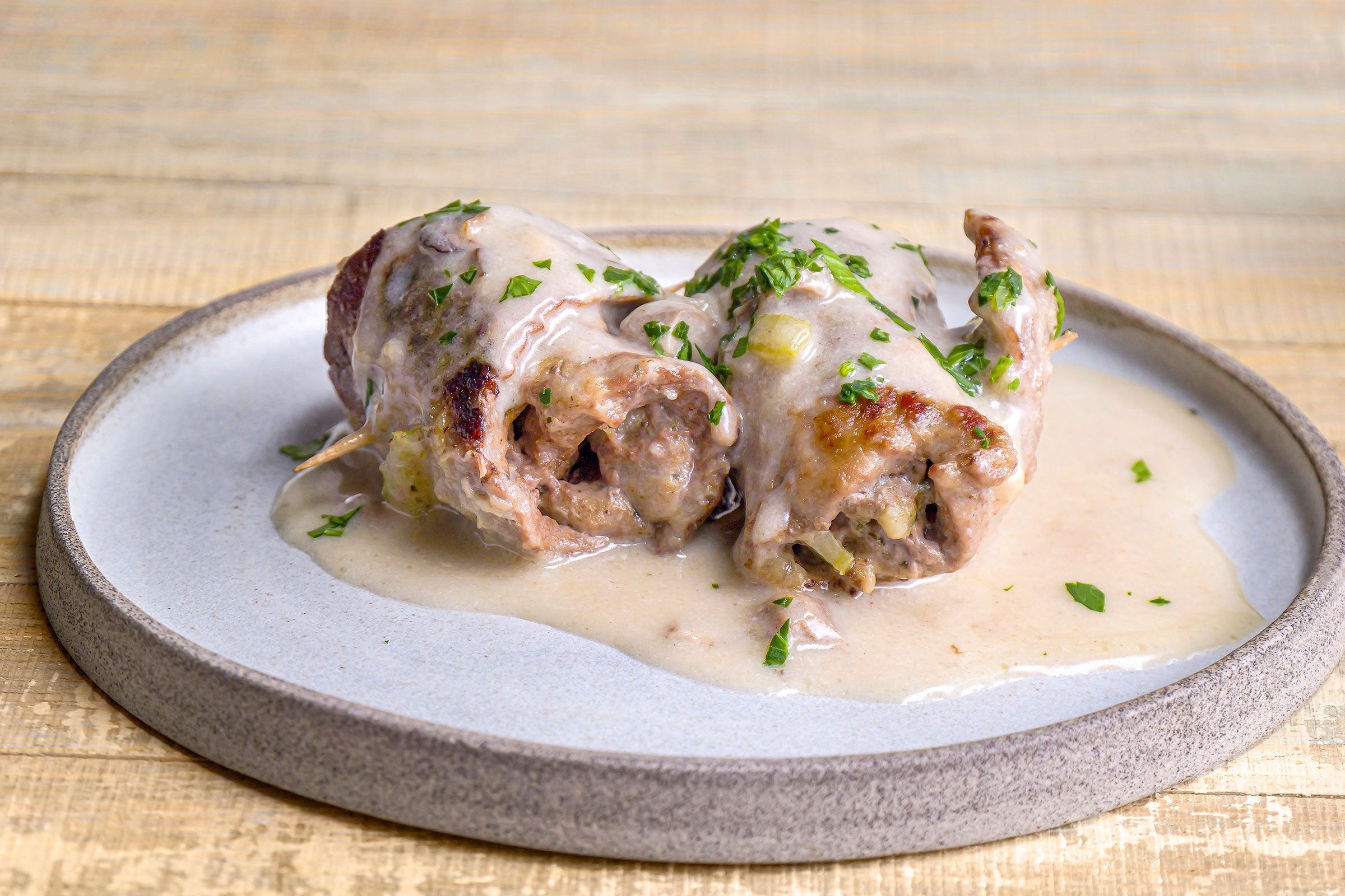 Steak Roll Ups served on a white plate with sauce poured over the rolls and some garnishing sprinkled.
