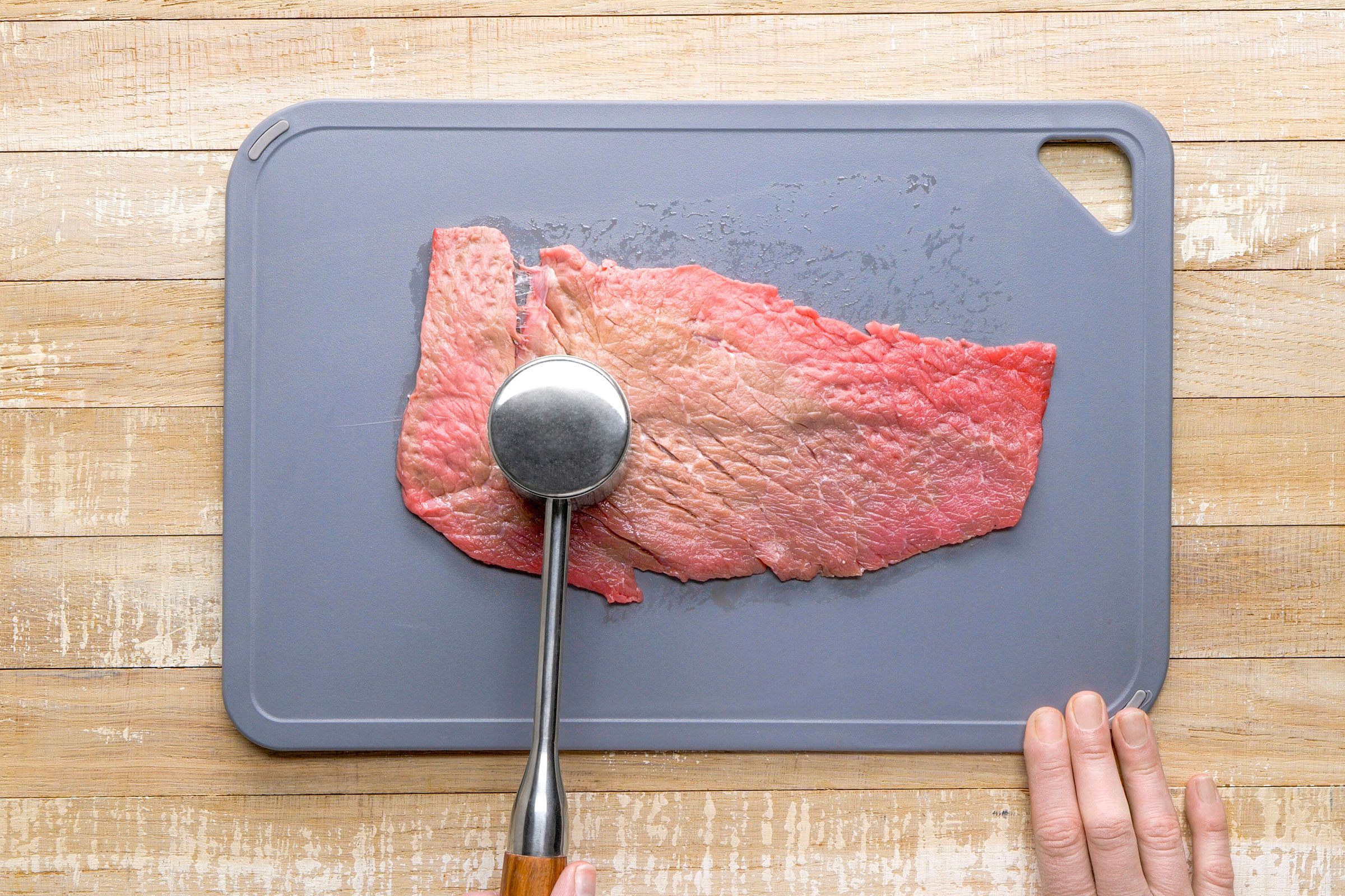 Using a meat mallet to flatten the steak to 1/3-inch thickness.
