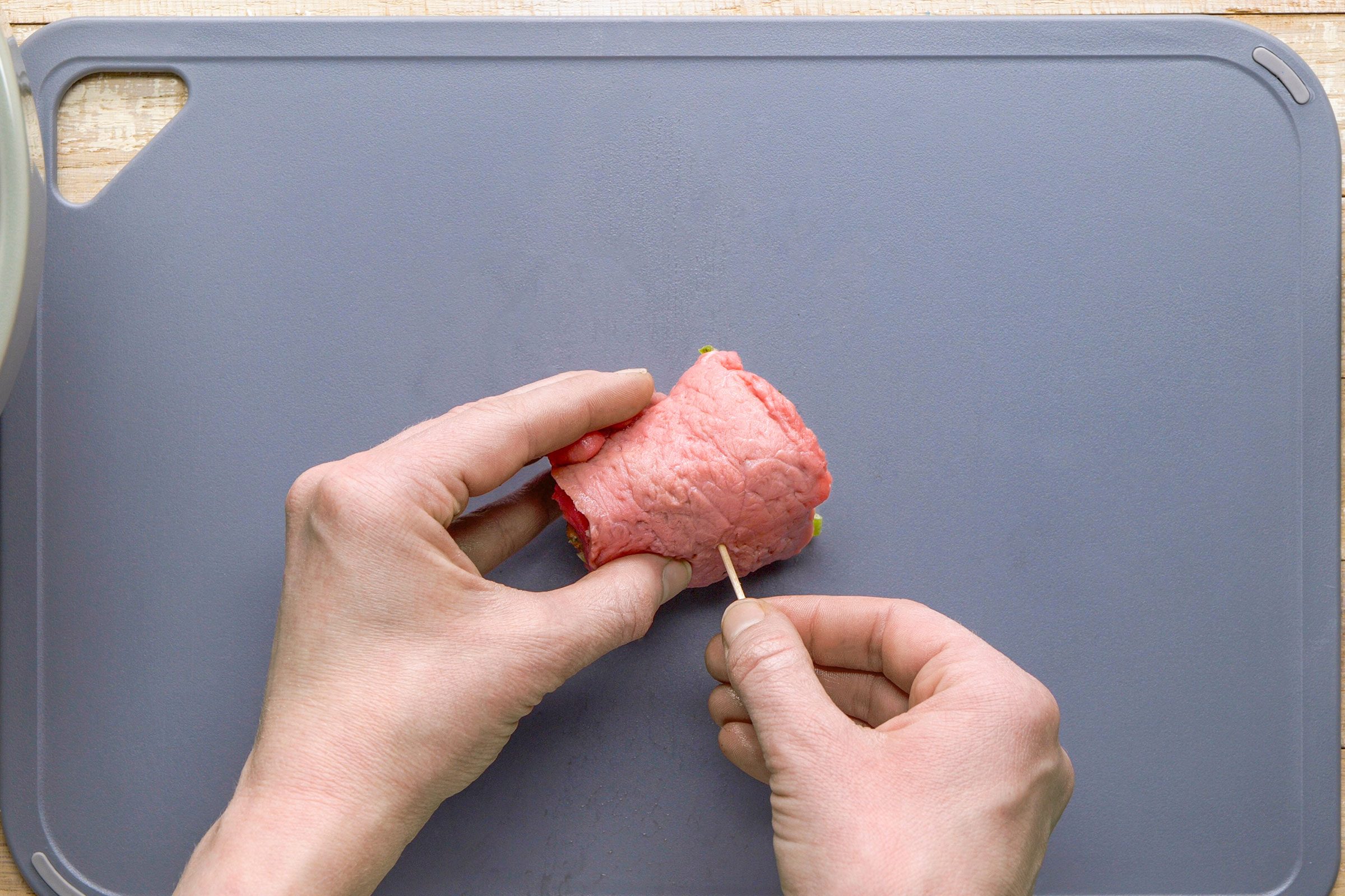 Rolling up a piece of meat with filling inside and securing it with a toothpick.