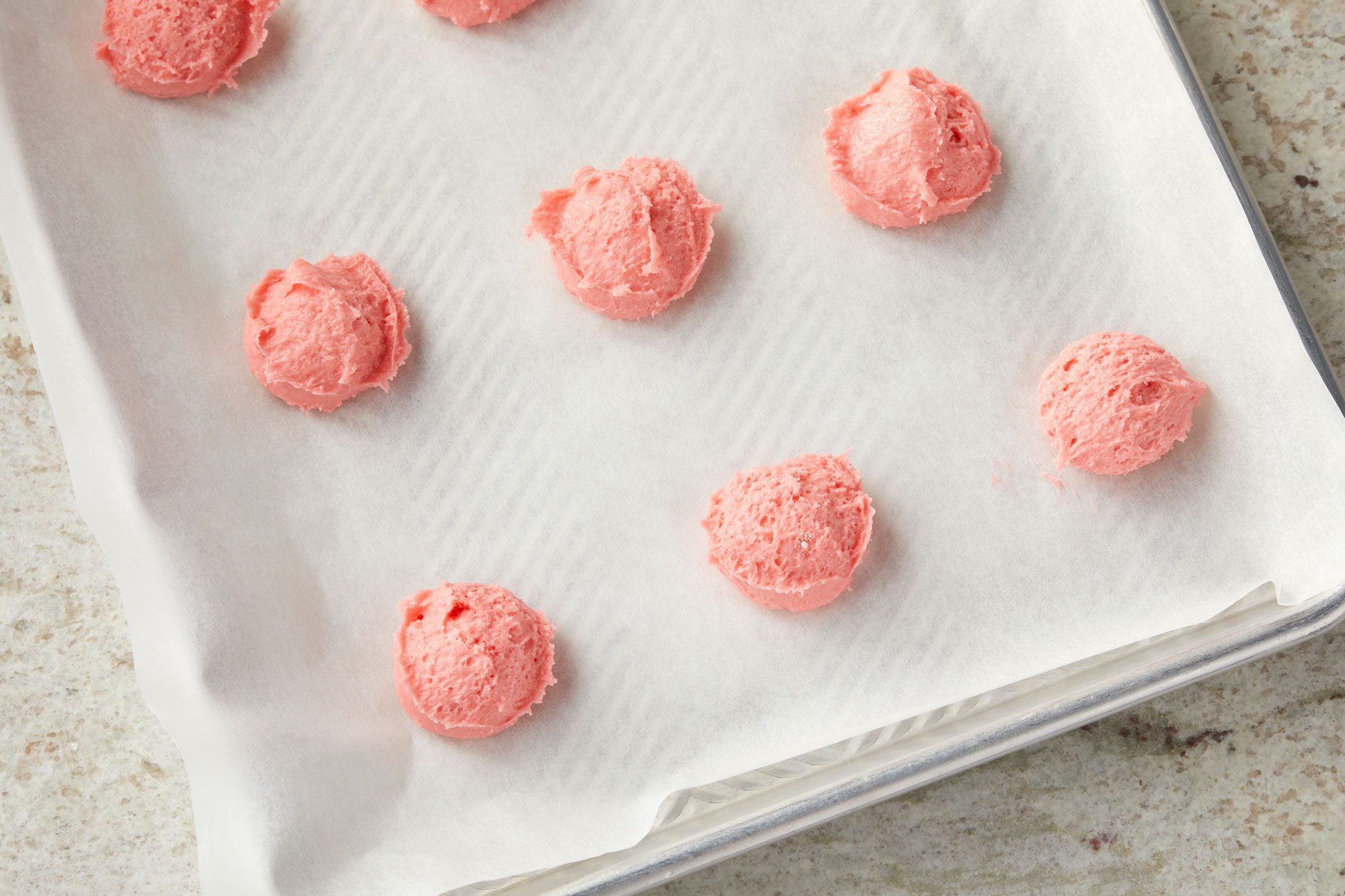Overhead shot of drop dough by tablespoonfuls 2-inch apart onto parchment-lined baking sheets; on a marble surface