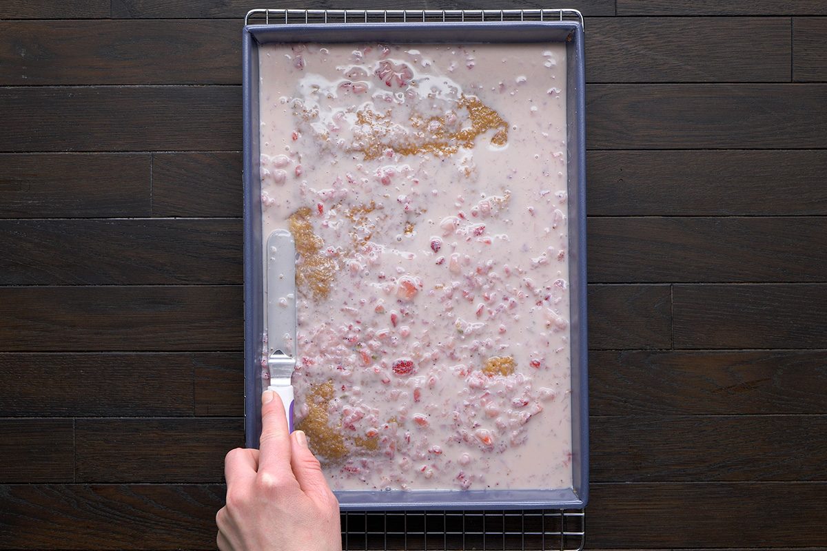 overhead shot of a rectangular baking tray filled with a strawberry mixture poured over cake