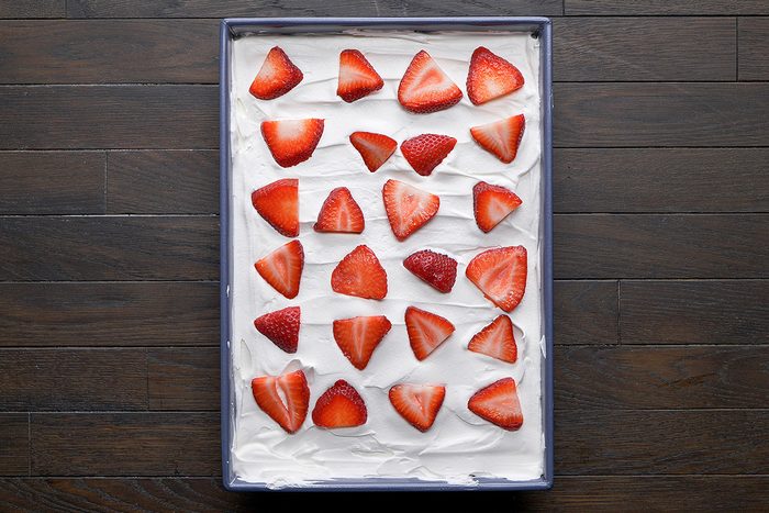 overhead shot of a rectangular tray filled with a smooth layer of creamy frosting, decorated with an arrangement of fresh strawberries on top