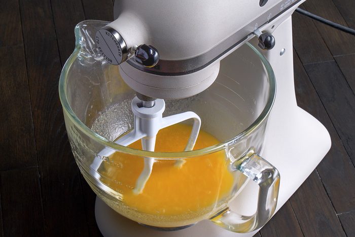3/4th shot of a stand mixer with glass mixing bowl that is partially filled with a vibrant yellow mixture