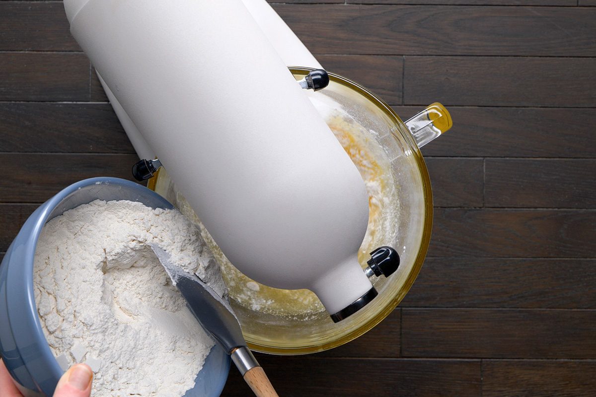 overhead shot of a hand is holding a blue bowl filled with flour added in the egg mixture