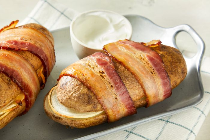 Close-up shot of Bacon-Wrapped Potatoes; served on a tray with choice of dip or sauce on a napkin; all set on a marble surface