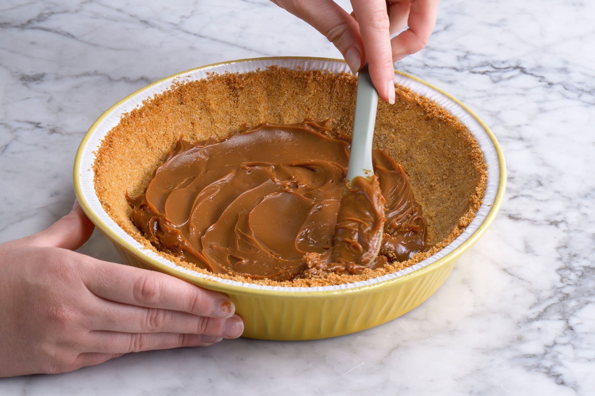 3/4 angle view shot of spread dulce de leche into cooled crust; on a marble textured surface