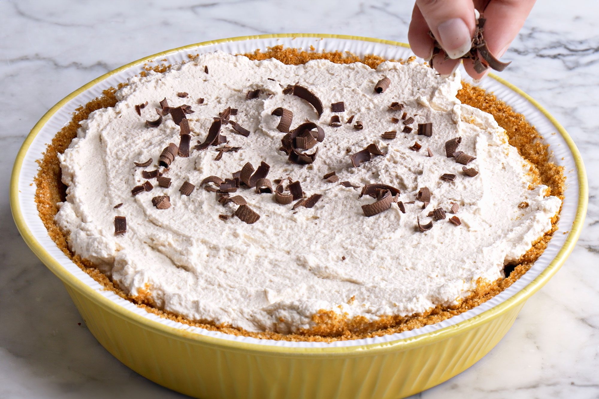 Close shot of the same pie plate; garnish with chocolate shavings before serving; alls et on a marble textured surface