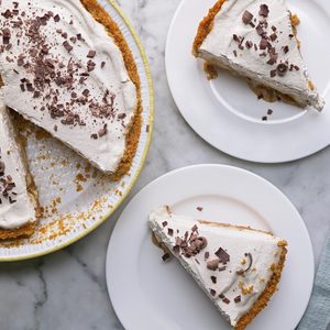 Overhead shot of Banoffee Pie in a large pie plate; sliced and served on two plates; with a fork resting on a light green napkin; all set on a marble-textured surface