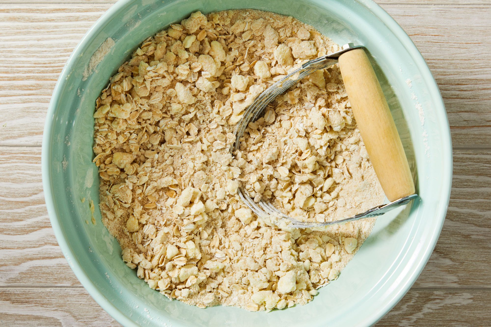 Overhead shot of a large bowl combine oats; brown sugar; flour and salt; stir well; Cut in butter until crumbly; Preheat oven to 350 degree; cream wooden surface