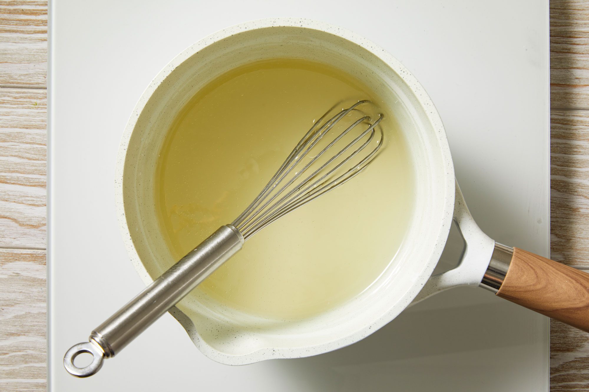 Overhead shot of a saucepan; combine sugar and cornstarch; stir in water; cook until mixture is thickened and clear; whisk tool; cream wooden surface