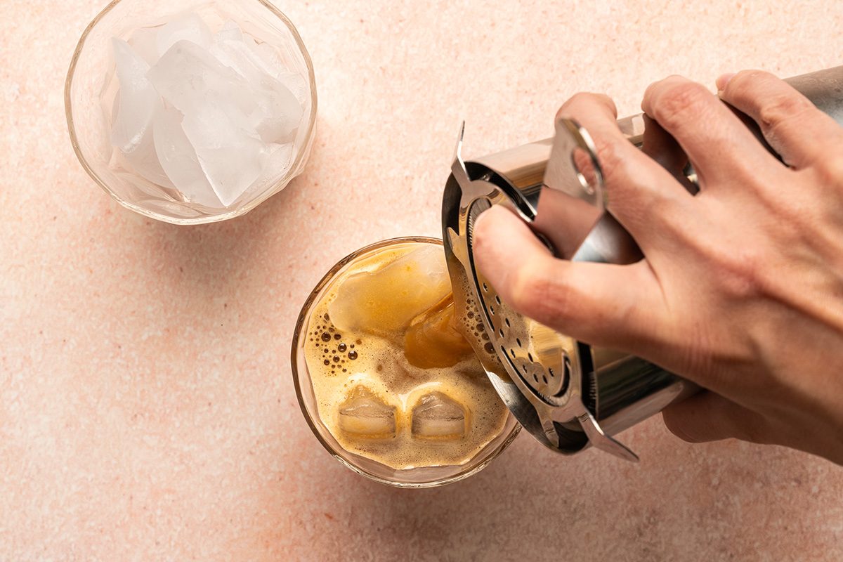 pouring coffee into the glass from shaker and another glass with ice is placed by the side