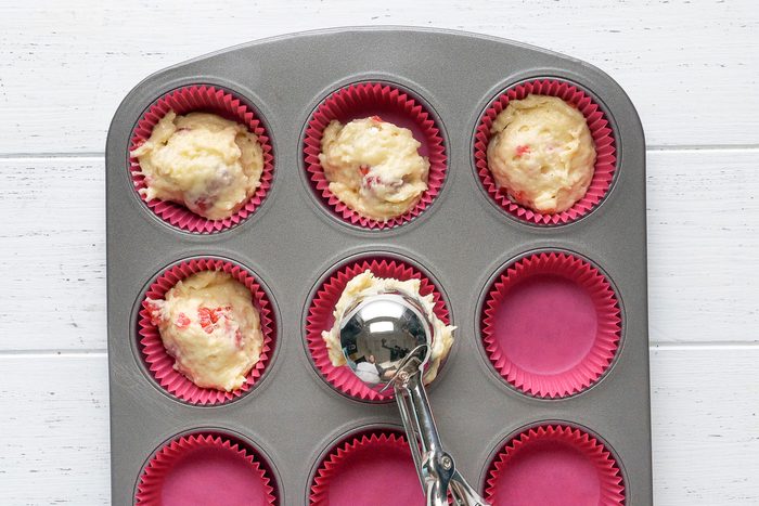 paper-lined muffin cups being filled about three-fourths full with the batter