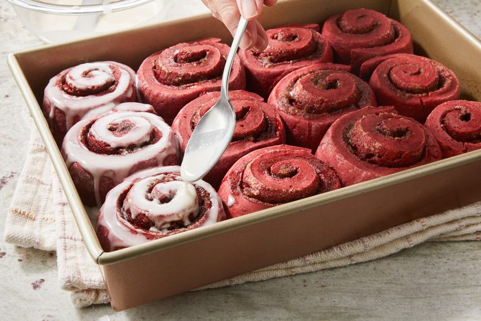 vanilla icing being spooned over baked rolls