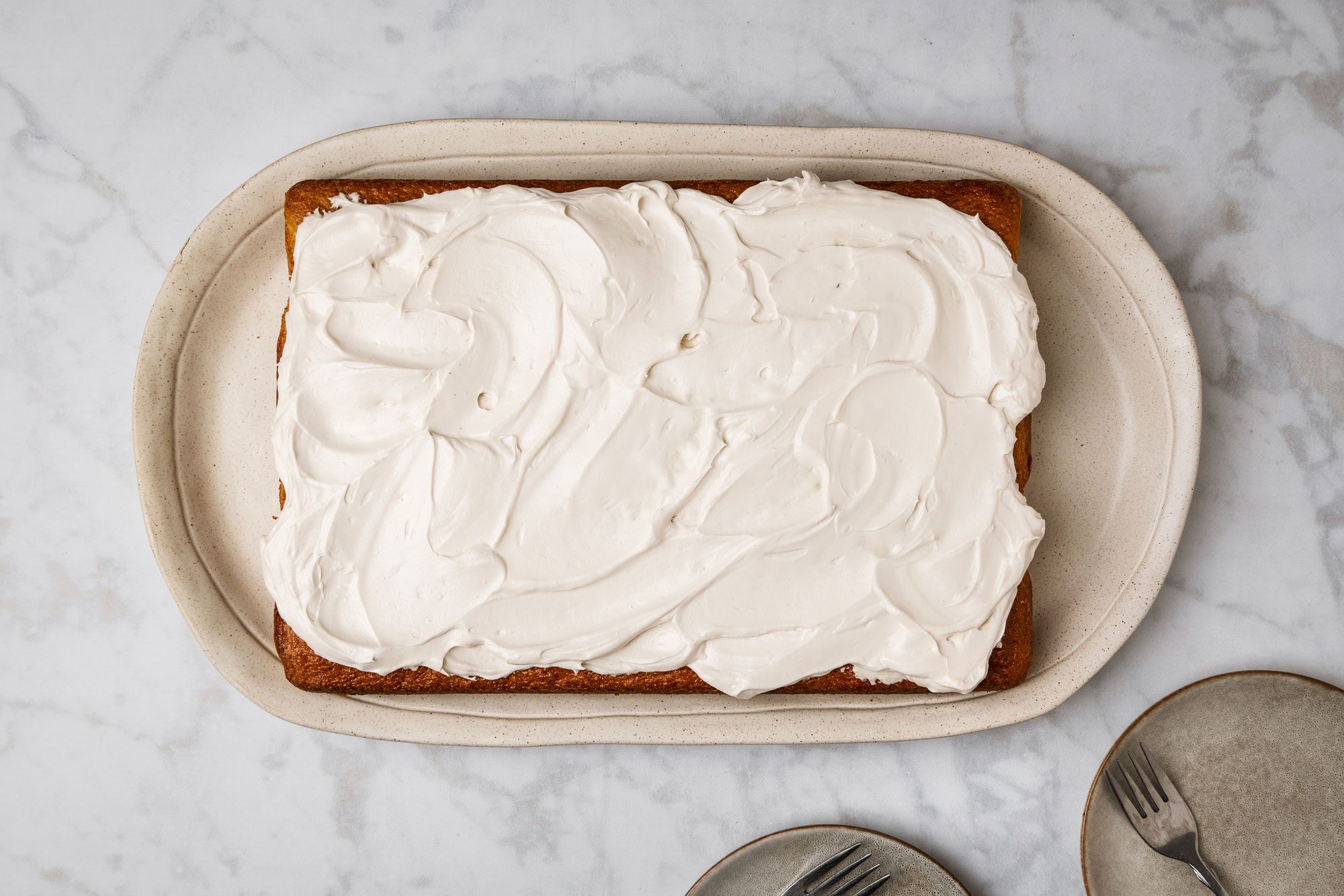 Overhead shot of Root Beer Float Cake in a baking pan; with two brown ceramic plates and forks neatly arranged nearby; all set on a marble surface