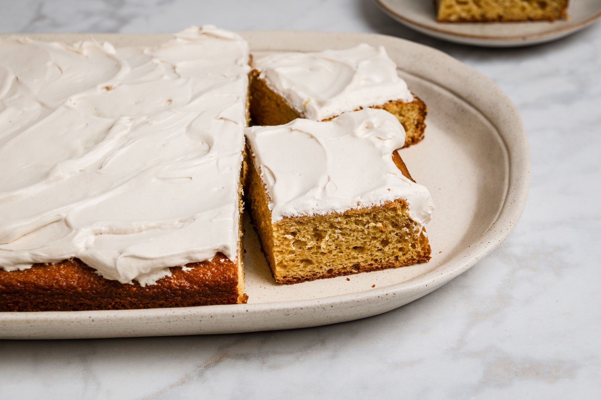 Close shot of Root Beer Float Cake in a baking pan; cut into slices and served on two brown ceramic plates; all set on a marble surface