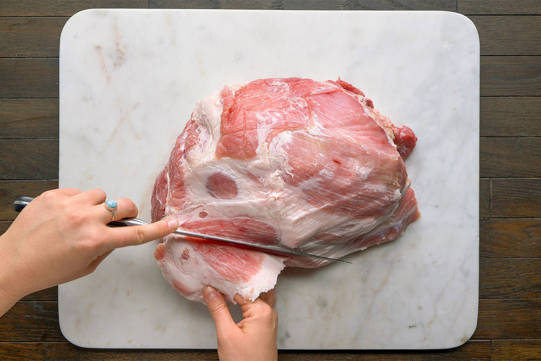 Overhead shot on a white cutting board on a table. Using a sharp knife; remove any fat on the outside of the ham.