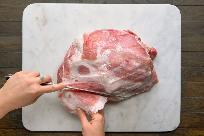 Overhead shot on a white cutting board on a table. Using a sharp knife; remove any fat on the outside of the ham.