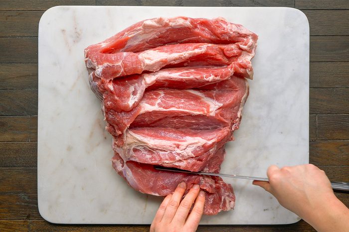Overhead shot on a white cutting board on a table. Lay ham flat; make 4 to 6 half moon slits into the deepest parks of the ham.