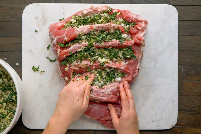 Overhead shot on a white cutting board on a table. Stuff mixture into ham, filling all gaps with your hands.