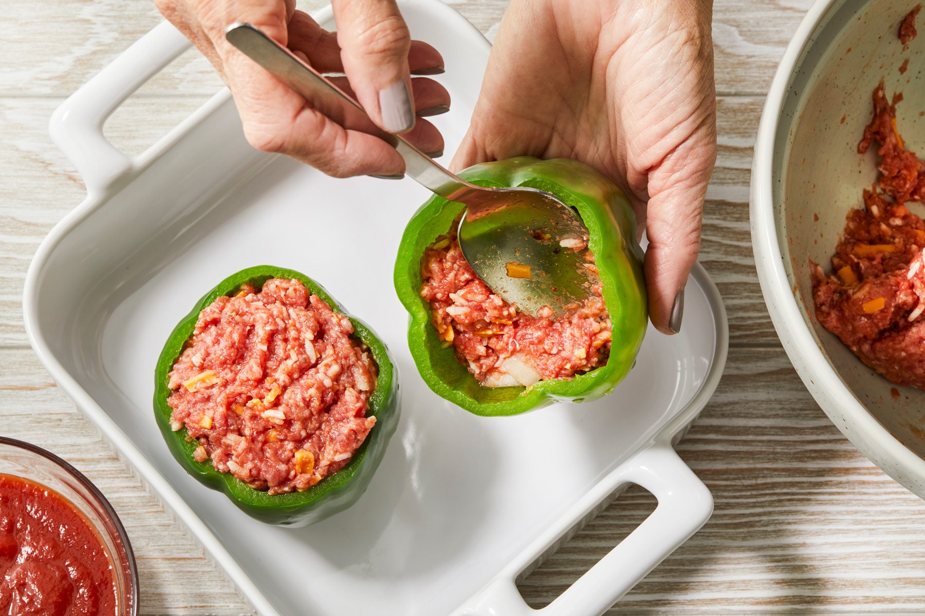 Overheda shot of Stuff the peppers; place in an ungreased 1-1/2-qt. baking dish; tomato sauce bowl is nearby; on a cream-colored wooden surface;