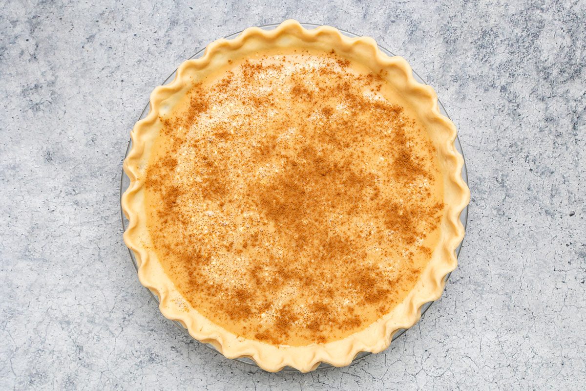Overhead shot of pour into the pie shell; sprinkle with cinnamon; bake at 425 degree for 10 minutes; reduce temperature to 350 degree; bake 35 minutes more or until a knife inserted in the center comes out clean; on a grey marble surface;