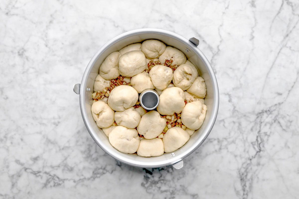 overhead shot of a bundt pan filled with unbaked dough balls, some nuts visible between the dough pieces, sits on a white marble surface