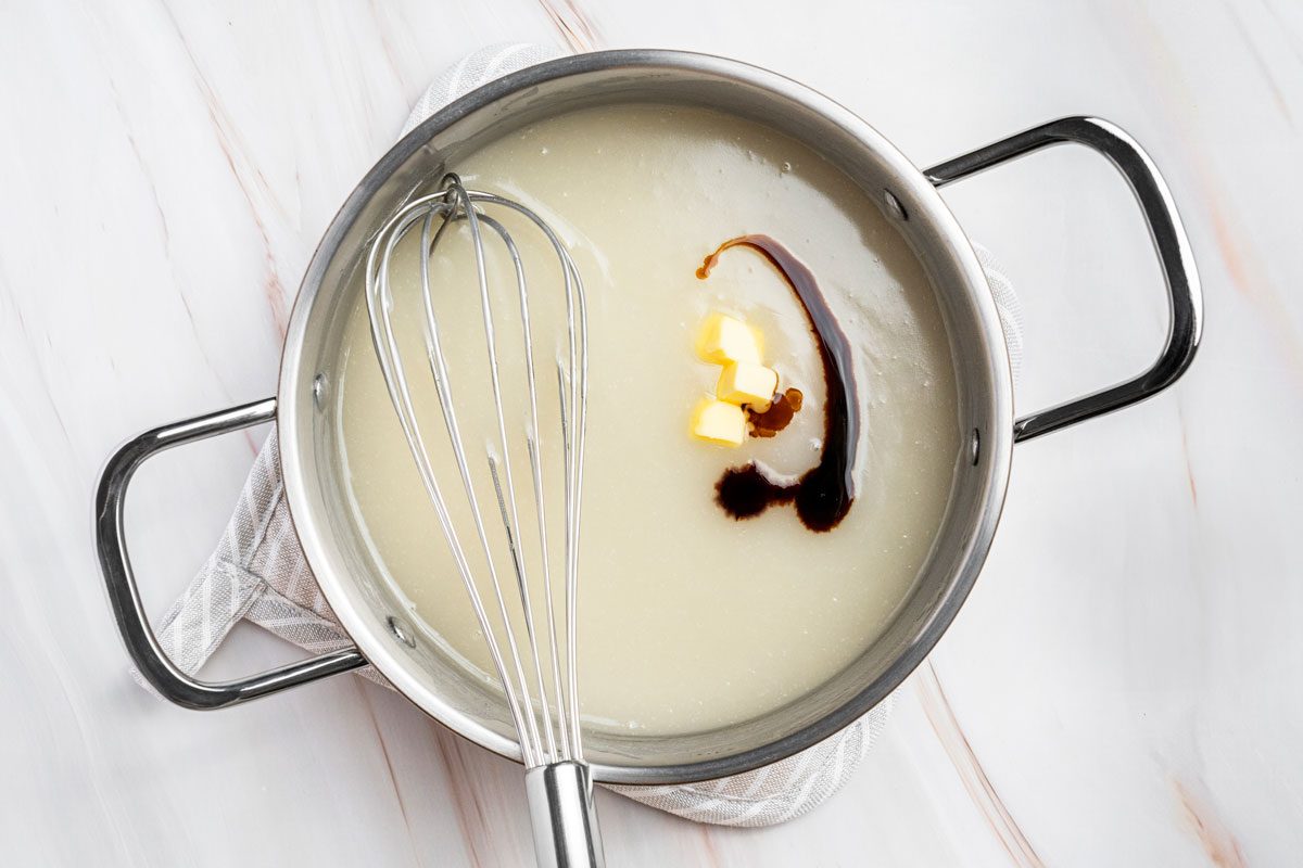 Overhead shot of stir in butter and vanilla; whisk tool; Cool to room temperature; all set on a marble surface;