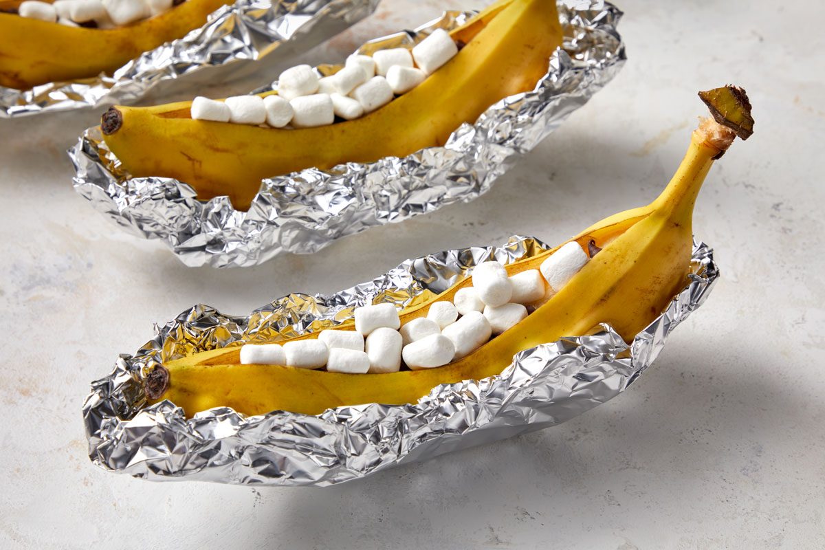 Close shot of Crimp and shape four pieces of heavy-duty foil around bananas; forming boats; Grill, covered, over medium heat until marshmallows melt and are golden brown 5-10 minutes; all set on a marble surface;