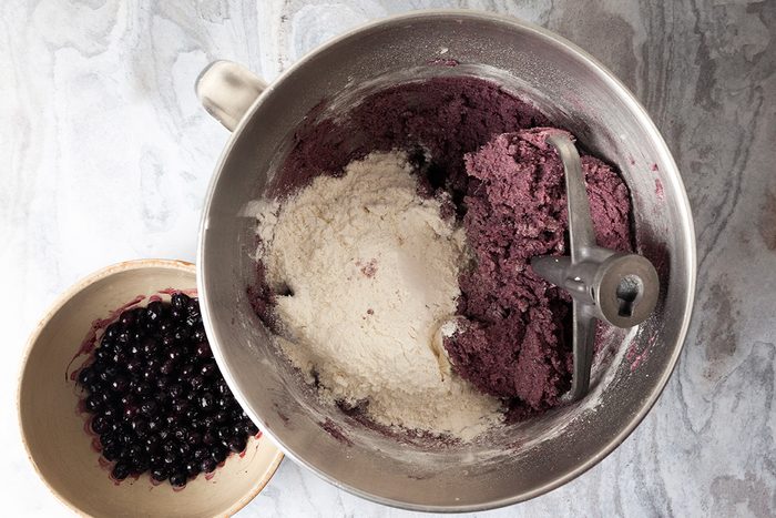 Overhead shot of small bowls; combine flour; baking powder and salt; add to the creamed mixture; beat on medium to low speed until just incorporated; fold in thawed wild blueberries; with juice; until incorporated; cover; refrigerate at least 2 hours; preheat oven to 400 degree; lace sugar in a shallow bowl; place confectioners sugar in a separate shallow bowl; scoop a rounded tablespoonful of the dough; gently roll into a ball; roll in sugar, then confectioners sugar; place on the baking sheet; repeat with remaining dough; spacing about 2 in; apart; all set on a marble surface;