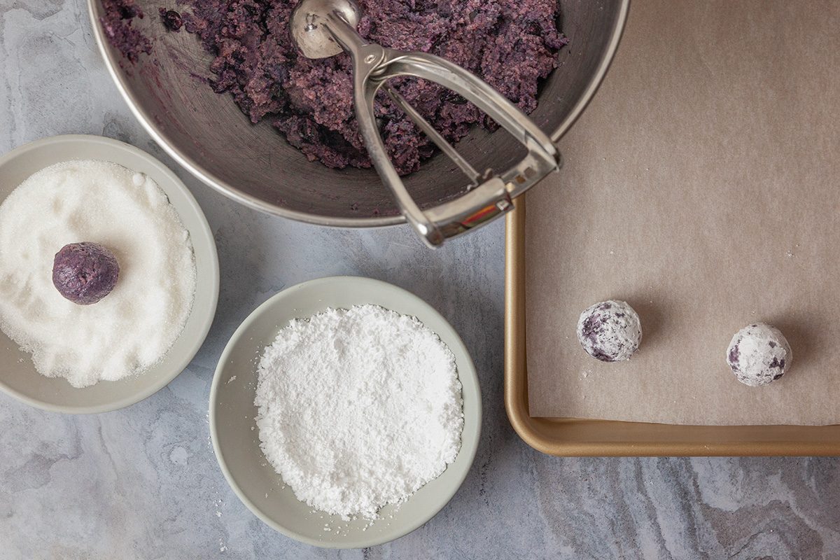 Overhead shot of small bowls; combine flour; baking powder and salt; add to the creamed mixture; beat on medium to low speed until just incorporated; fold in thawed wild blueberries; with juice; until incorporated; cover; refrigerate at least 2 hours; preheat oven to 400 degree; lace sugar in a shallow bowl; place confectioners sugar in a separate shallow bowl; scoop a rounded tablespoonful of the dough; gently roll into a ball; roll in sugar, then confectioners sugar; place on the baking sheet; repeat with remaining dough; spacing about 2 in; apart; all set on a marble surface;