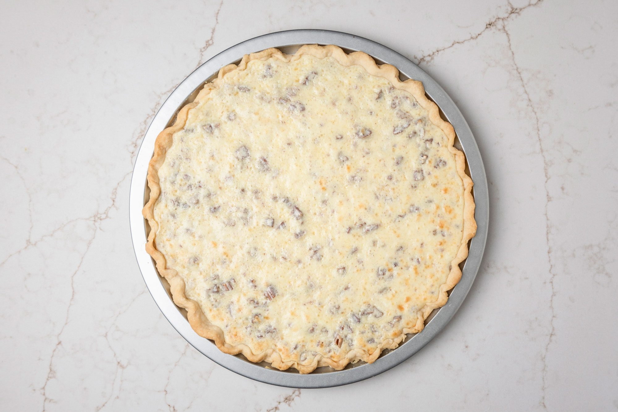 Overhead shot of a pie palte; In a large bowl beat cream cheese and sugar until smooth; Beat in eggs and vanilla; Stir in nuts; Spread over crust; Bake 10 minutes longer; Cool; Drain cherries; reserving 1/3 cup juice; Set cherries and juice aside; all set on a white texture marble surface