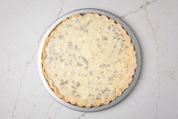 Overhead shot of a pie palte; In a large bowl beat cream cheese and sugar until smooth; Beat in eggs and vanilla; Stir in nuts; Spread over crust; Bake 10 minutes longer; Cool; Drain cherries; reserving 1/3 cup juice; Set cherries and juice aside; all set on a white texture marble surface