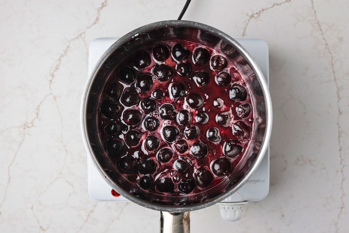 Overhead shot of a large saucepan combine sugar and cornstarch; stir in reserved juice until smooth; add cherries; Cook and stir over medium heat until mixture comes to a boil; Cook and stir 2 minutes longer; Remove from the heat; stir in butter; extract and food coloring; Cool to room temperature; all set on a white texture marble surface