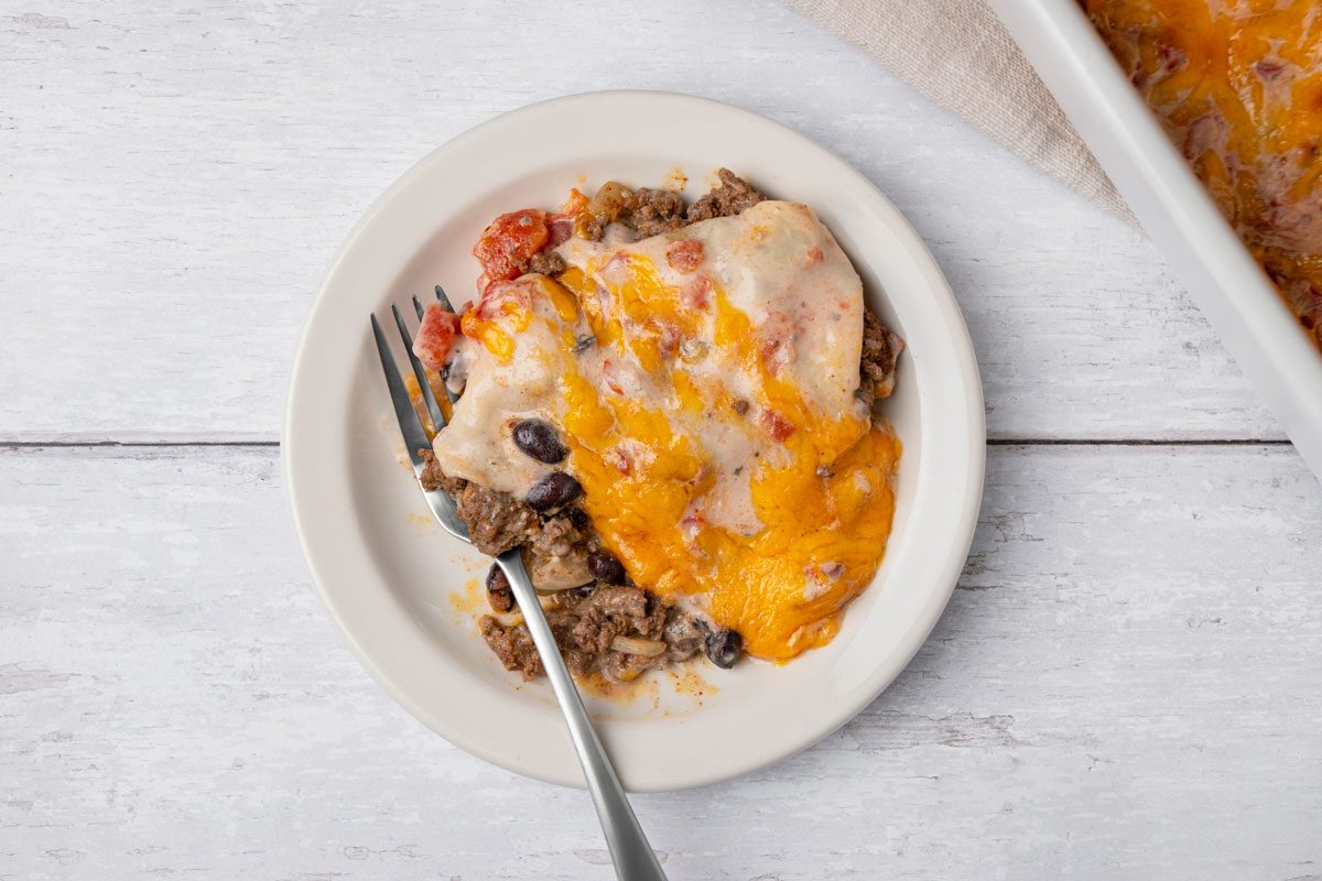 Top view shot of Firecracker Casserole in a baking dish; served on a small plate with a fork; all set on a white wooden surface;
