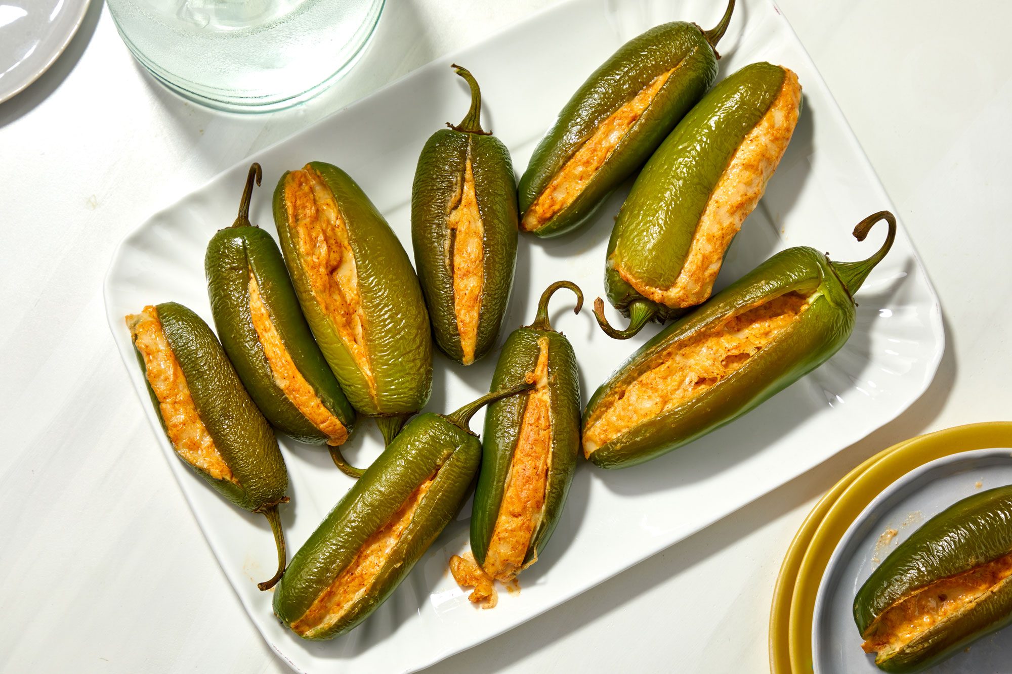 Overhead shot of Grilled Stuffed Jalapenos serve warm on a large white platter; with plates; all set on a white surface