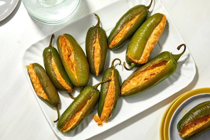 Overhead shot of Grilled Stuffed Jalapenos serve warm on a large white platter; with plates; all set on a white surface