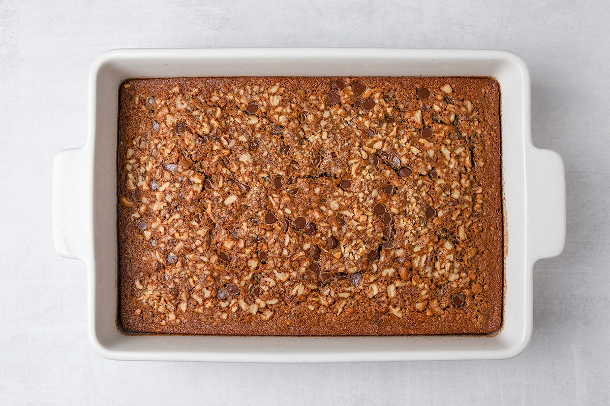 A baked oatmeal casserole with a golden-brown, crumbly oat topping is shown in a rectangular white baking dish on a light background.