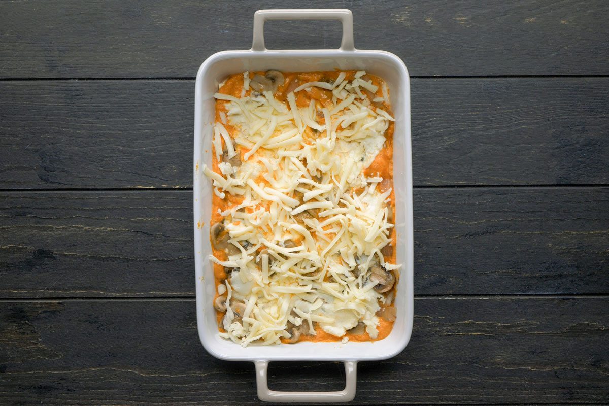 Top Shot of A rectangular white baking dish holds a cheesy casserole with sliced mushrooms on top; the dish sits on a dark wooden surface
