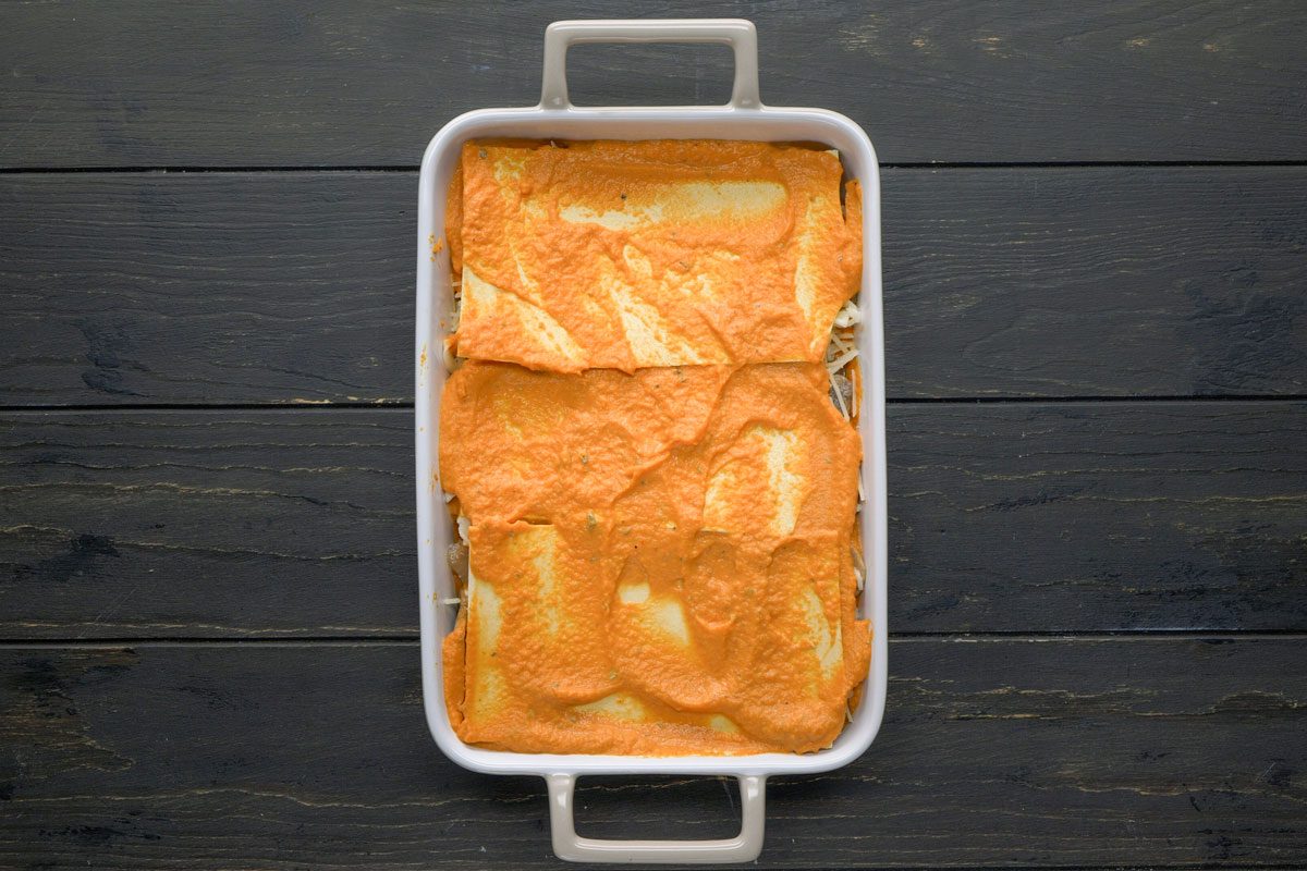 Top Shot of A white rectangular baking dish holds neatly arranged enchiladas, smothered in orange enchilada sauce atop a dark wooden surface, highlighting contrast; the presentation emphasizes warmth and rustic dining