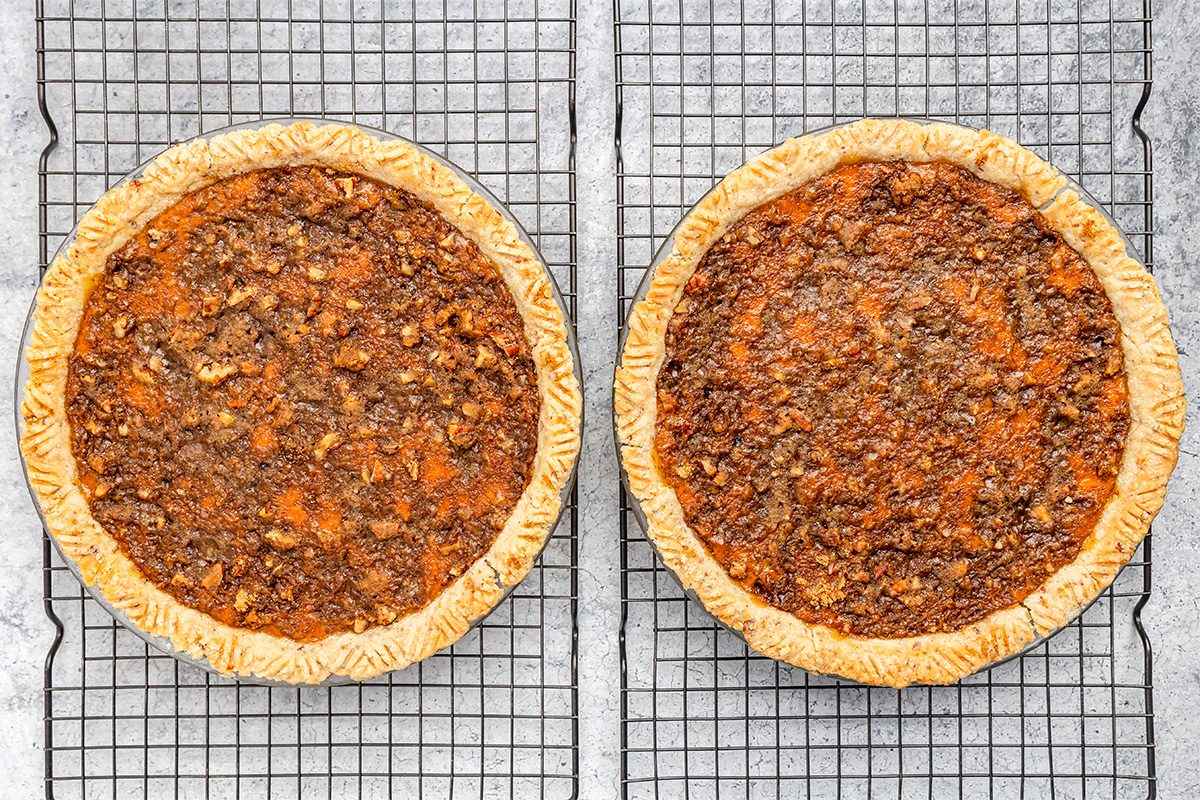 Two pecan pies with golden-brown crusts and nutty, textured tops are cooling on wire racks placed on a light gray surface.