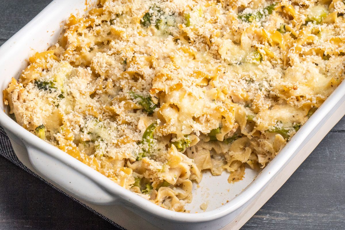 3/4th shot of a white casserole dish holds baked noodles; broccoli; and is topped with golden-brown melted cheese and crispy breadcrumbs; creating a comforting meal; Tuna Broccoli Casserole;