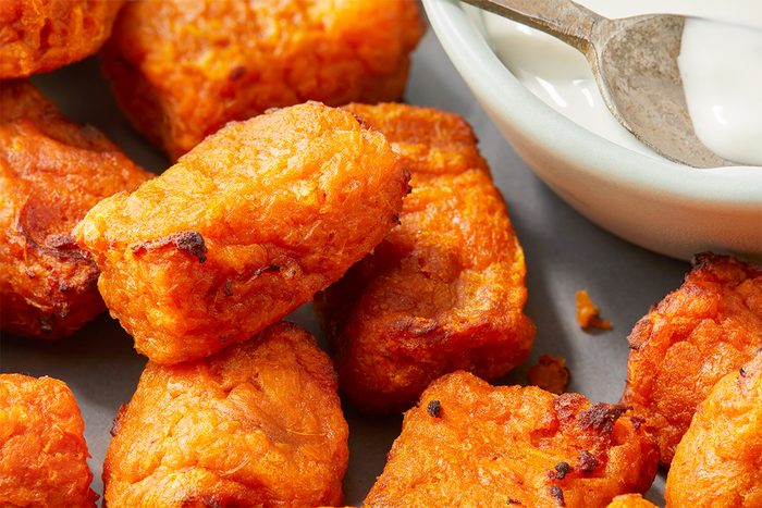 Close-up of crispy, golden-brown tater tots arranged near a small bowl of creamy white dipping sauce with a spoon.