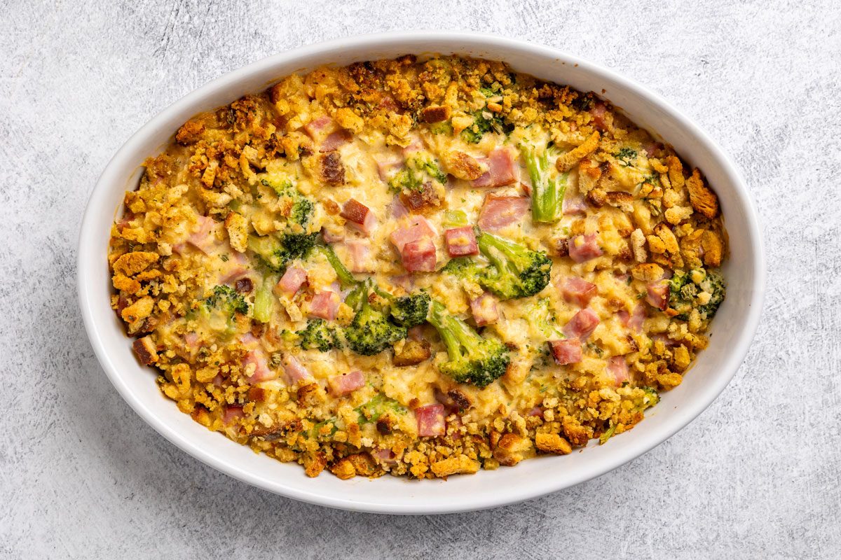 Top-down shot; baked casserole in white oval dish; golden breadcrumbs; ham chunks; broccoli florets; melted cheese; light surface